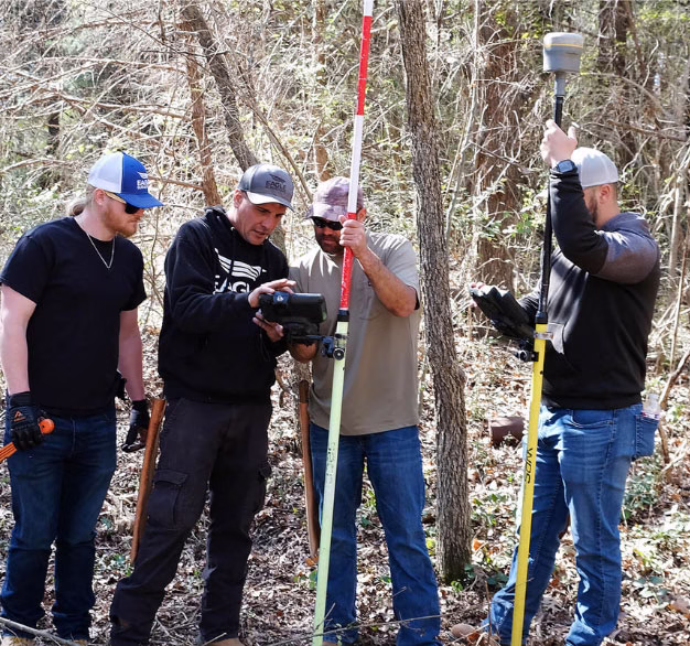 four surveyors in a wooded area with transit
